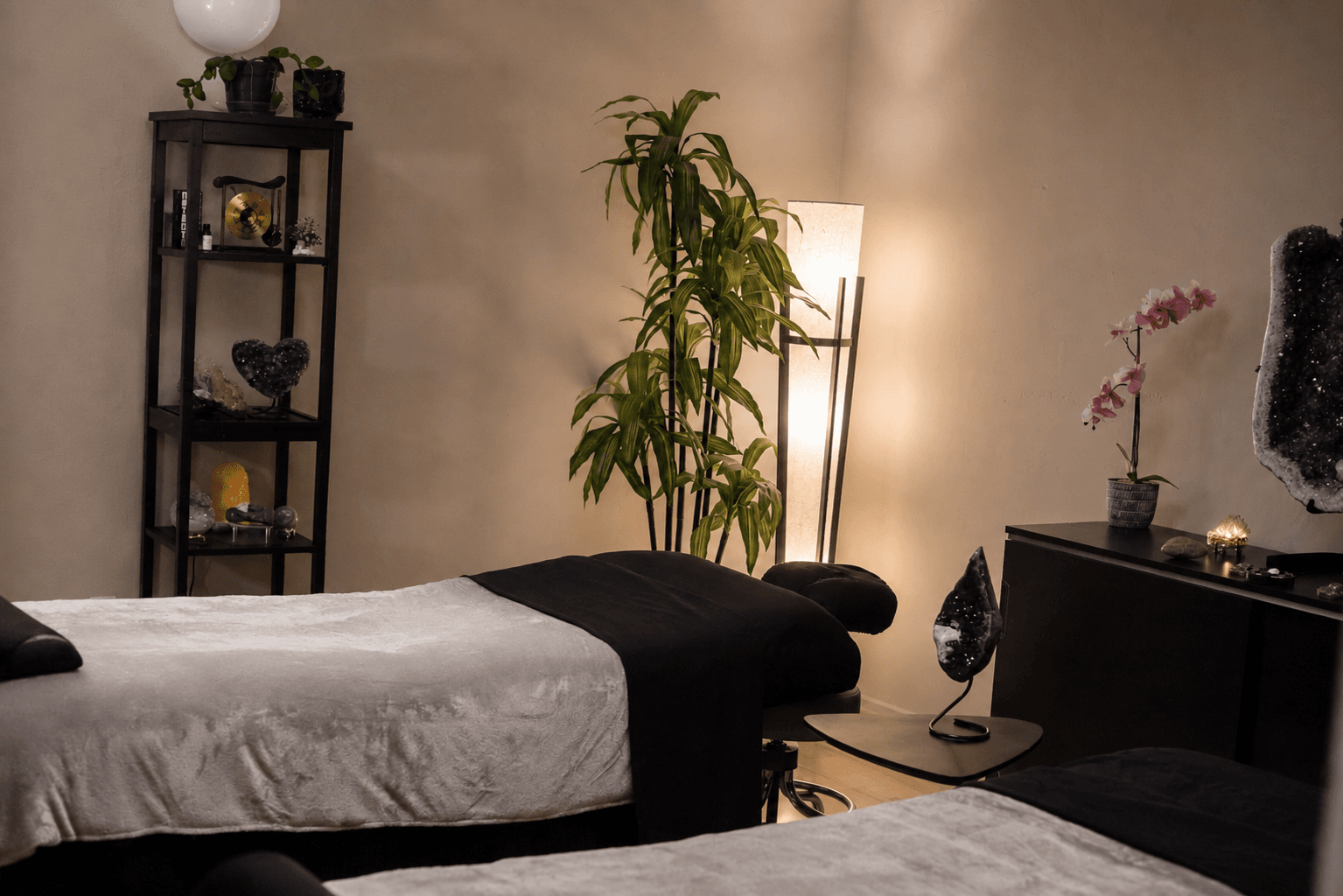 A softly lit private wellness treatment room at Sedonya with two massage tables, plants, and crystals