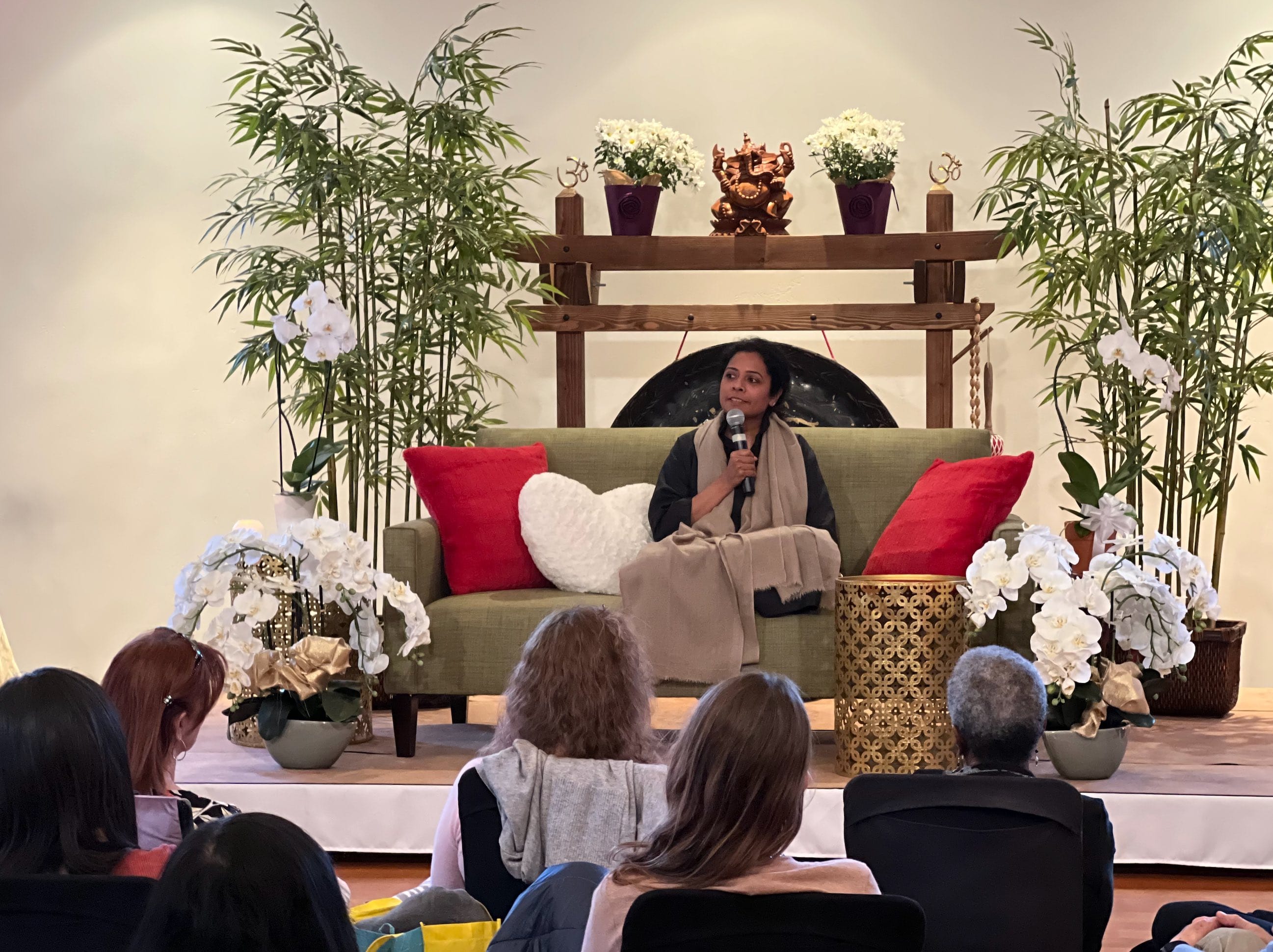 A speaker sharing with a seated audience from the Cathedral's green sofa, surrounded by bamboo and the ceremony gong
