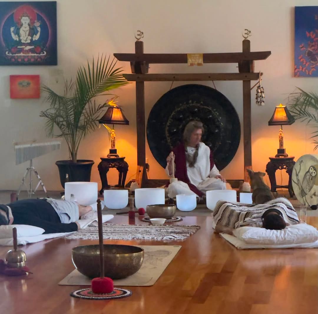 A gong and sound bath ceremony with singing bowls, guests resting on mats beneath a wooden torii altar