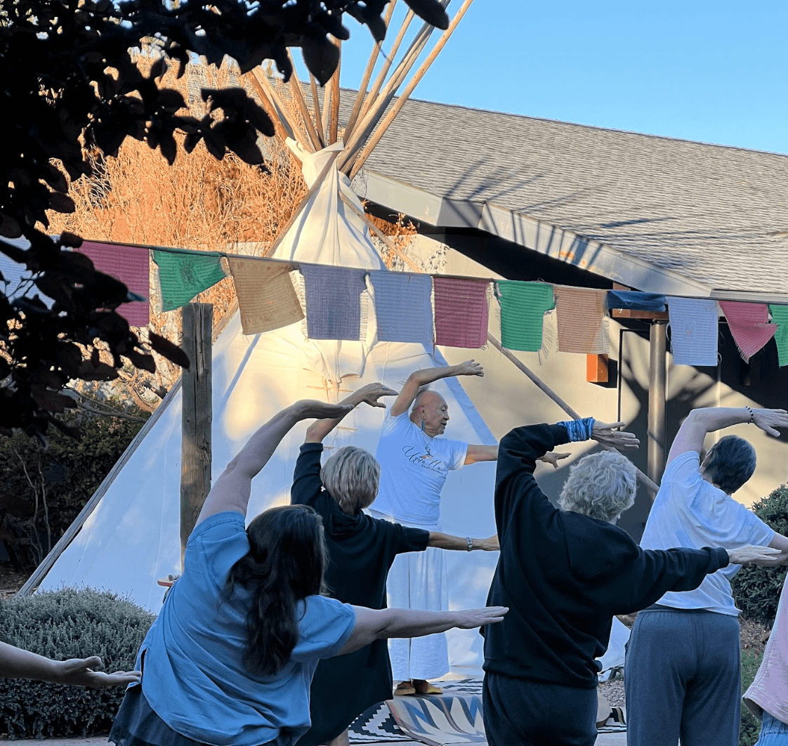 Guests moving through a sunrise qigong sequence in front of the tipi, led by Uqualla in white